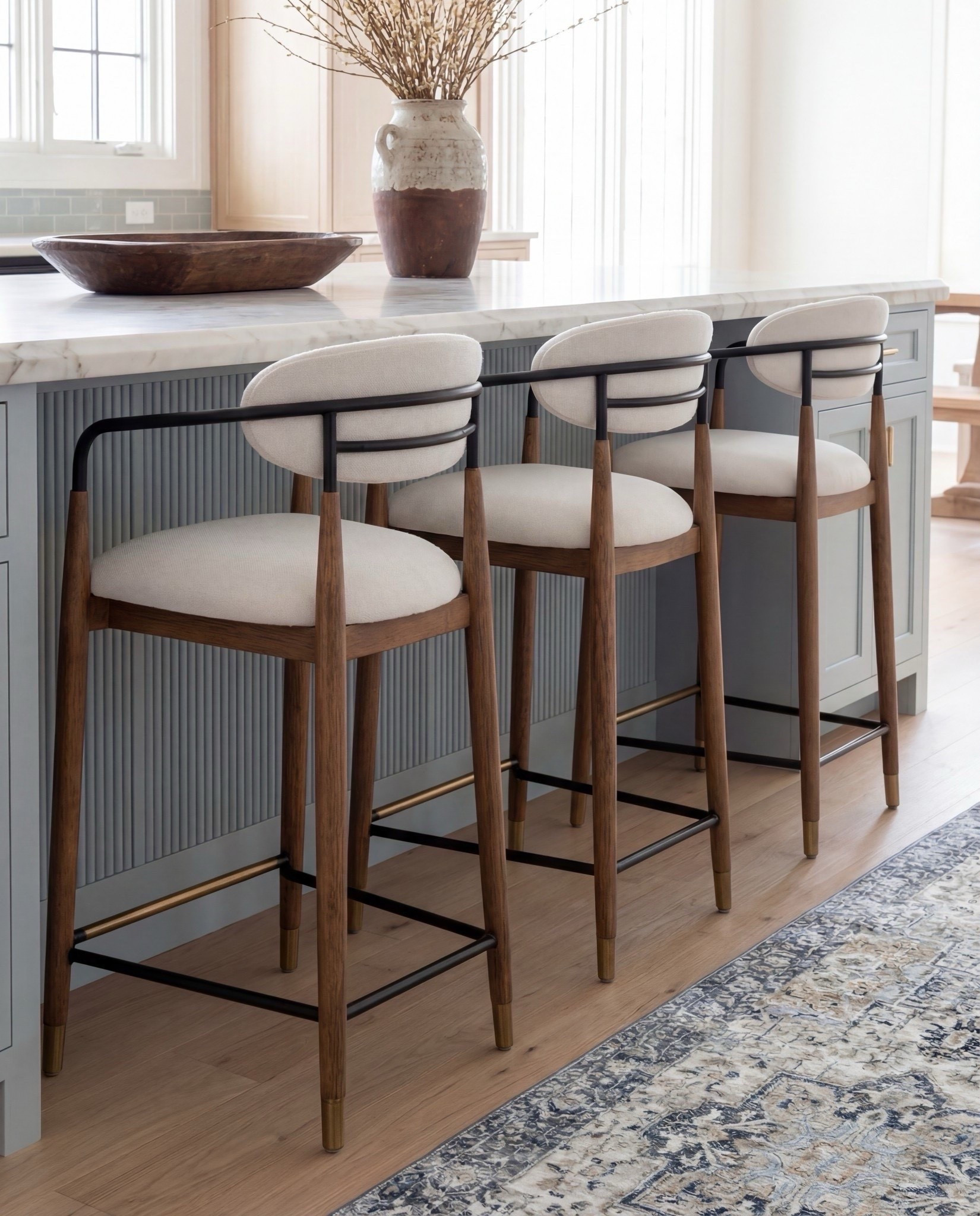 Shop the Look:
• Light blue fluted kitchen island
• Warm oak kitchen cabinets
• Brass globe pendant lights
• Marble kitchen countertop
• Neutral blue patterned runner
• Black + brass bar stools
• Soft blue subway tile backsplash
• Brown Ceramic vase with branches
• Gold kitchen faucet and hardware
•Brown bowl 
Brown floral wall art
Black candle holder

#LTKSaleAlert #LTKHome