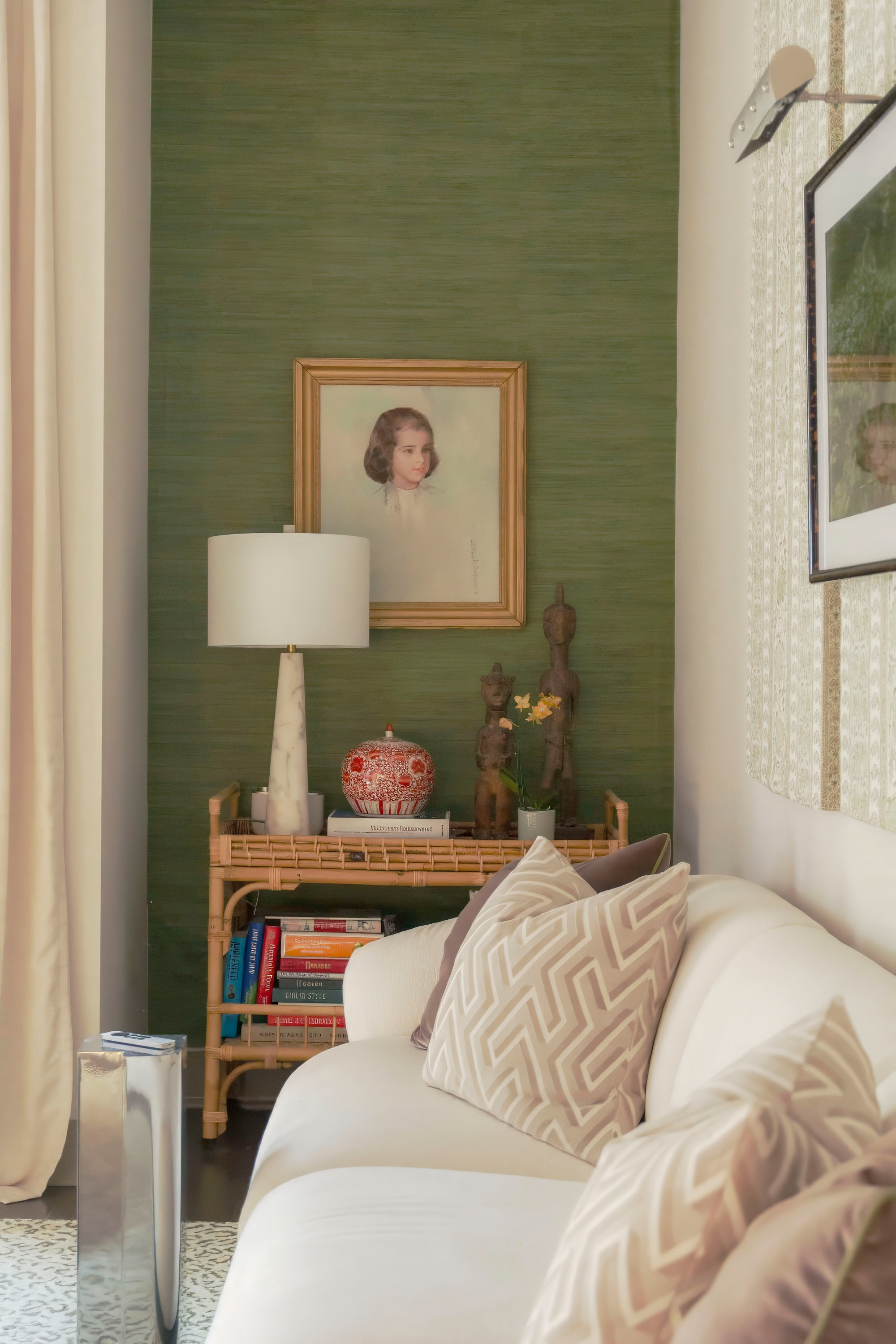 Chic modern living room styling with layered textures and timeless details. This cozy corner features a neutral white sofa with geometric throw pillows, a sleek marble table lamp, bamboo side table, and curated decorative accents. The green grasscloth accent wall creates depth, while framed artwork and sculptural pieces add character and warmth. A perfect blend of contemporary design and classic home decor inspiration for a sophisticated yet inviting space. 

 