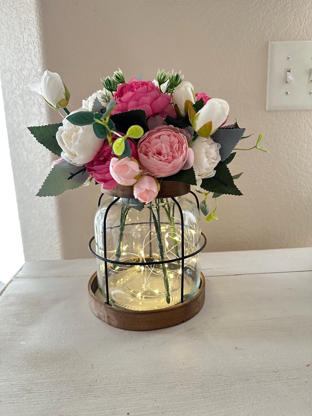 Charming and versatile, this vintage-inspired jar lantern is the perfect accent to style through every season. Designed with removable florals and soft LED fairy lights on a timer, it creates a cozy glow while giving you the flexibility to switch up your look year-round. Whether placed on a table, shelf, or entryway, this piece adds a warm, nostalgic touch with just the right hint of farmhouse charm. #LTKhome #homedecor #farmhousestyle #cozylighting #lanterndecor #seasonalstyle #decorinspo #cozyhome

#LTKHome #LTKWedding #LTKSeasonal