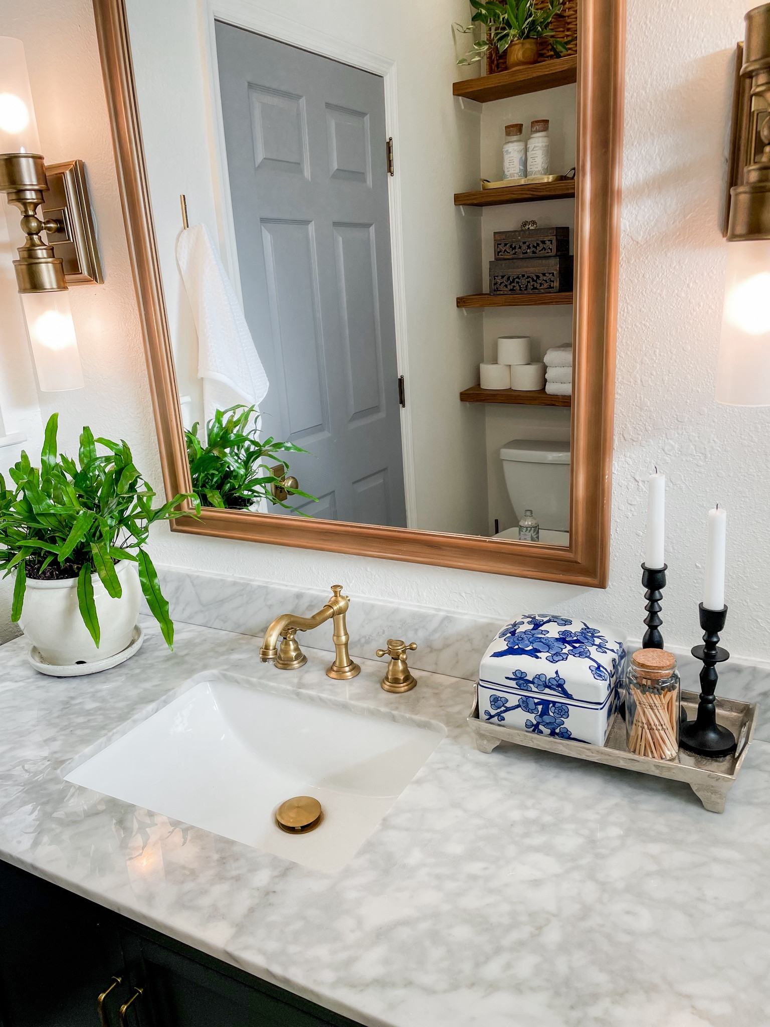 Bathroom remodel done in gray and white marble with dark blueish grey vanity, brass finishes and side lights, mixed with wood mirror.  

Brass faucet, brass lighting sconces. 

#LTKhome