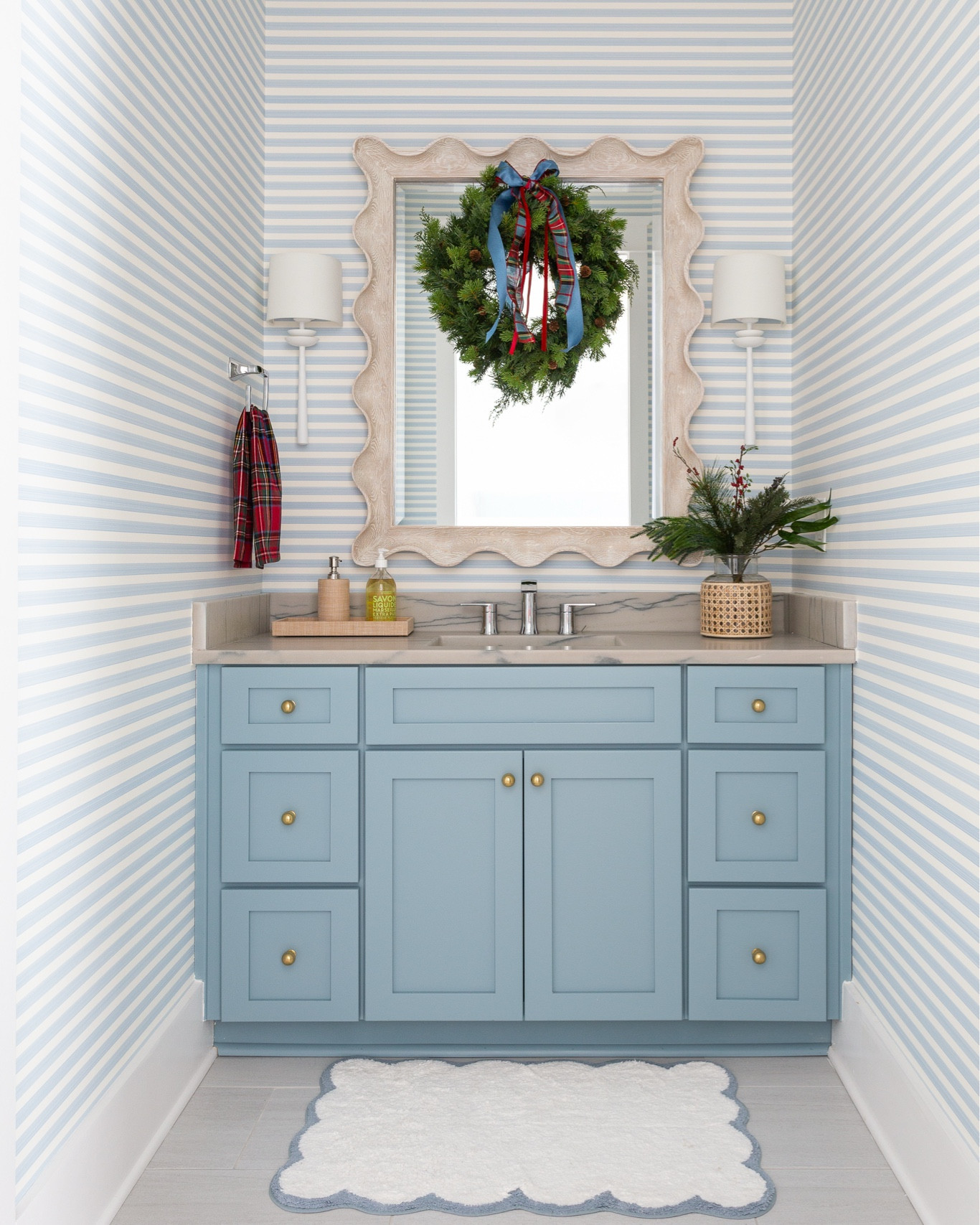 Our light blue striped bathroom decorated for Christmas! We love the gold knobs on our blue cabinets, blue striped wallpaper, scalloped bath mat, faux evergreen bundle, cane wrapped vase, wreath with ribbons, and plaid hand towel! Also linking our white sconces and scalloped wood mirror. See the full tour here: https://lifeonvirginiastreet.com/2024-christmas-home-tour/.
.
#ltkhome #ltkseasonal #ltksalealert #ltkstyletip #ltkfindsunder50 #ltkfindsunder100 coastal decor, coastal fall decorating ideas #LTKsalealert #LTKhome

#LTKHoliday #LTKSaleAlert #LTKHome
