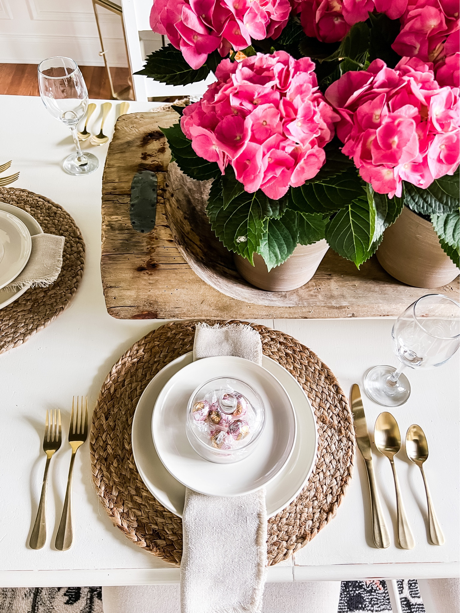 Style a beautiful and simple table! Woven placemats warm up white dinnerware. Gold flatware and wine glasses add some sparkle. Fringed linen napkins. A sweet treat nestled under a glass cloche. This huge dough bowl filled with hydrangea plants is a stunning but easy centerpiece. #tablescape #hydrangea 

#LTKSeasonal #LTKstyletip #LTKhome