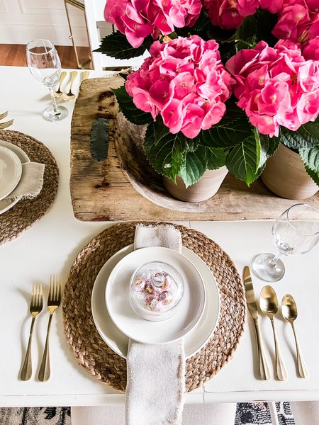 Style a beautiful and simple table! Woven placemats warm up white dinnerware. Gold flatware and wine glasses add some sparkle. Fringed linen napkins. A sweet treat nestled under a glass cloche. This huge dough bowl filled with hydrangea plants is a stunning but easy centerpiece. #tablescape #hydrangea 

#LTKSeasonal #LTKstyletip #LTKhome
