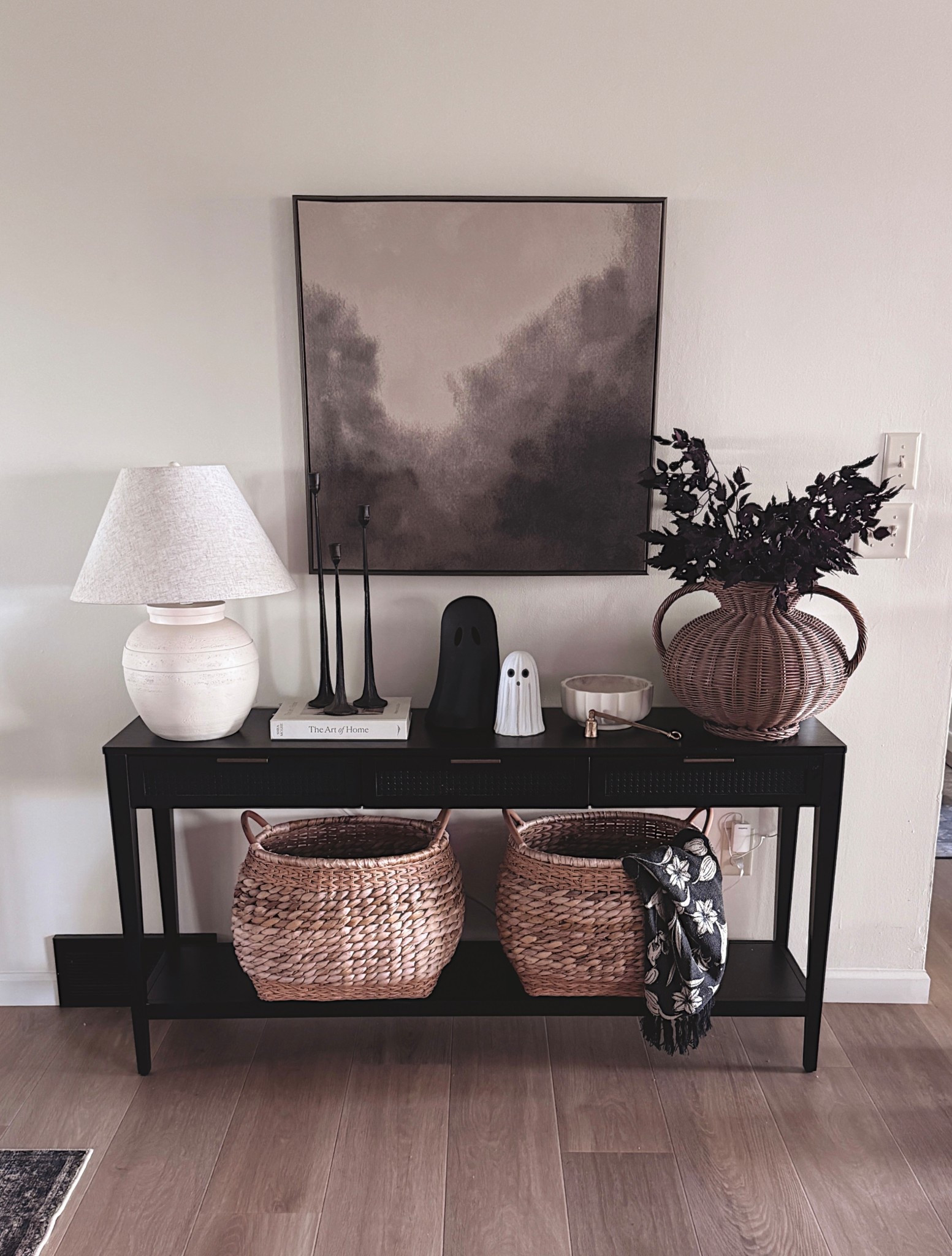 Neutral fall entryway vibes 🍂🖤 Mixing woven textures, cozy baskets, moody stems, and just a touch of Halloween with my favorite little ghost candles 👻 Everything is linked for you — from the black console to the wicker baskets + all the cozy details. #LTKhome #FallDecor #ConsoleTableStyling #LTKSeasonal