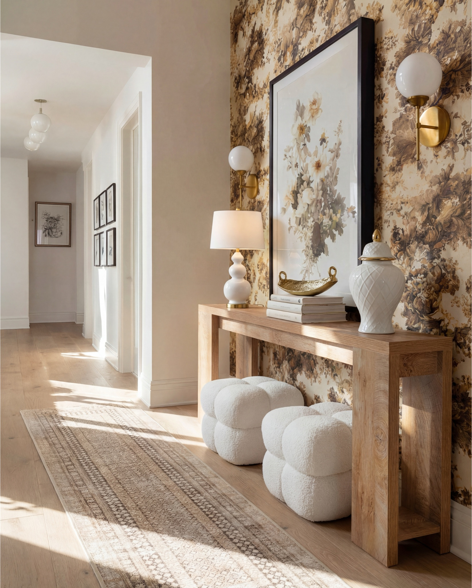 Warm, welcoming, and just a little bit glam — this foyer sets the mood the second you walk in. The tones stay soft and neutral, but the textures and patterns make everything feel elevated and thoughtfully layered.

The light wood console adds that effortless organic feel and gives the perfect styling moment. I layered a glossy sculptural lamp, a floral art piece with moody drama, and a few favorite decor objects to keep the vignette curated but still personal.

Those boucle pouf stools tucked underneath? Perfect for extra seating while keeping the walkway wide and open. Plus, the texture is such a cozy touch in a high-traffic space.

The runner introduces subtle pattern underfoot while keeping everything calm and cohesive. And the floral wallpaper — it brings warmth, depth, and just enough vintage charm to make the space unforgettable.

✨ Shop the Look
Light wood console table | White boucle pouf stools | Sculptural white table lamp | Gold accent decor bowl | Large floral framed artwork | Neutral patterned hallway runner | Warm floral wallpaper | Brass globe sconces

#LTKFindsUnder100 #LTKHome #LTKSaleAlert