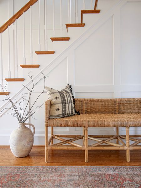 The is plenty of space below the staircase to style a bench or console table. 
This is the rattan Shore bench from Serena and Lily. Am Artisan vase from Pottery Barn is to the left  

#LTKhome #LTKstyletip #LTKFind