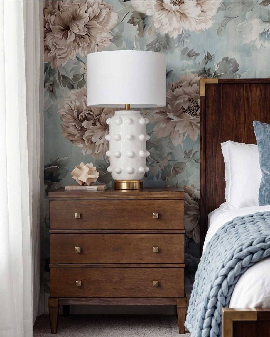 There’s just something about a moody, layered bedroom that feels instantly grounding, and this space captures that balance of warmth and sophistication perfectly. Every detail works together to create a cozy, elevated retreat.

The rich walnut bed anchors the room with its clean lines and warm tone, softened by the chunky blue knit throw and plush layered pillows. I love how the deeper wood frame contrasts with the soft floral wallpaper — it makes the entire wall feel like a curated backdrop.

The nightstands echo the darker wood tones while the sculptural white lamps bring in that playful, elevated texture. They add just enough contrast to keep the look fresh and modern.

The terracotta bench at the foot of the bed introduces a warm pop that ties back to the copper tones in the oversized artwork above. A simple knitted throw draped over the bench adds softness and warmth.

The vintage-style rug pulls everything together with its muted blues, soft creams, and subtle patterning. It’s the perfect foundation for a bedroom that leans cozy but still feels refined.

✨ Shop the Look
Walnut bed frame | Chunky knit throw | Textured white table lamps | Floral wallpaper | Terracotta bench | Layered blue and neutral pillows | Vintage-inspired rug | Oversized copper artwork

#LTKsale #LTKhome #LTKstyletip