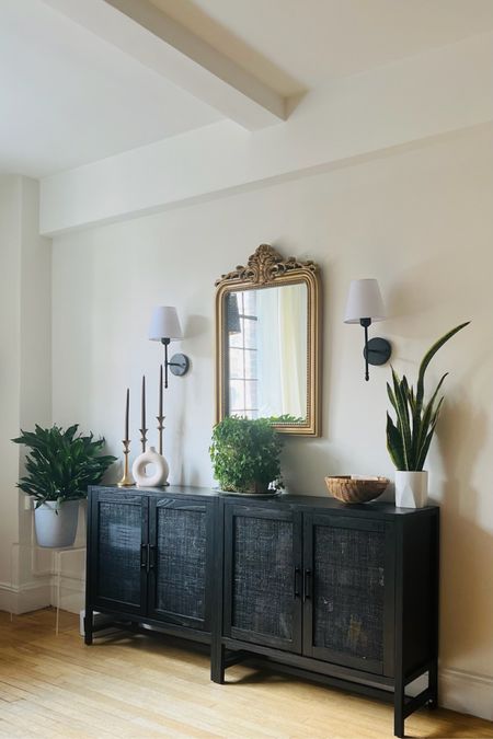This NYC apartment received a glow up just by adding a few accessories like this gold mirror and battery operated sconces to the cabinet they already owned! #blacksideboard #goldmirror #svonces