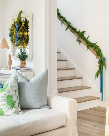 Our simple coastal Christmas decor includes blue and green pillows on our linen sofa, garland on our staircase with green and blue velvet ribbon, a light wood console table decorated with a light wood nutcracker, rattan table lamp, small Christmas tree, prelit wreath, and velvet ribbon! See our full Christmas home tour here: https://lifeonvirginiastreet.com/2022-christmas-home-tour/. 

#ltkhome #ltkholiday #ltkseasonal #ltksalealert #ltkstyletip #LTKHoliday #LTKhome #LTKsalealert #ltkfindsunder50 #ltkfindsunder100

#LTKhome #LTKsalealert #LTKHoliday