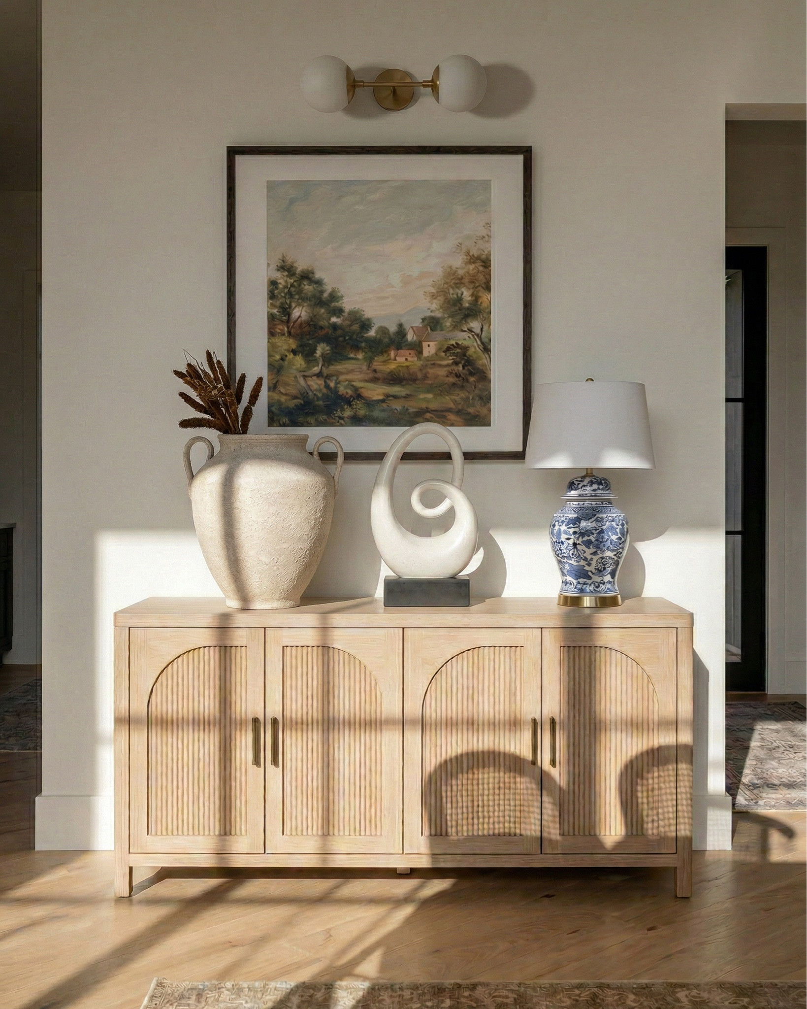 * Rectangular light wood dining table (traditional trestle base)
* Woven cane dining chairs (natural oak frame)
* Neutral vintage-style area rug (distressed pattern)
* Brass modern chandelier (linear / sculptural arms)
* Rustic exposed wood ceiling beams (reclaimed look)
* Large black-framed sliding glass doors (industrial style)
* Dark ceramic vase (handmade / organic texture)
* Dried floral arrangement (neutral stems)
* Sculptural brass decorative bowl
* Black ceramic candle holder (modern abstract form)
* White taper candle
* Small matte black decorative bowl
* Minimalist sculptural object (black accent piece)
* Light wood sideboard cabinet (fluted / ribbed detailing)
* Built-in arched niche cabinet (custom millwork look)
* Decorative pottery (neutral ceramic vases)
* Framed landscape wall art (classic / muted tones)
* Indoor olive tree (or faux olive tree)
* Neutral linen / textured textiles
* Warm light oak flooring
* Soft cream / off-white wall paint
* Arched doorway architectural detail


#LTKSaleAlert #LTKHome