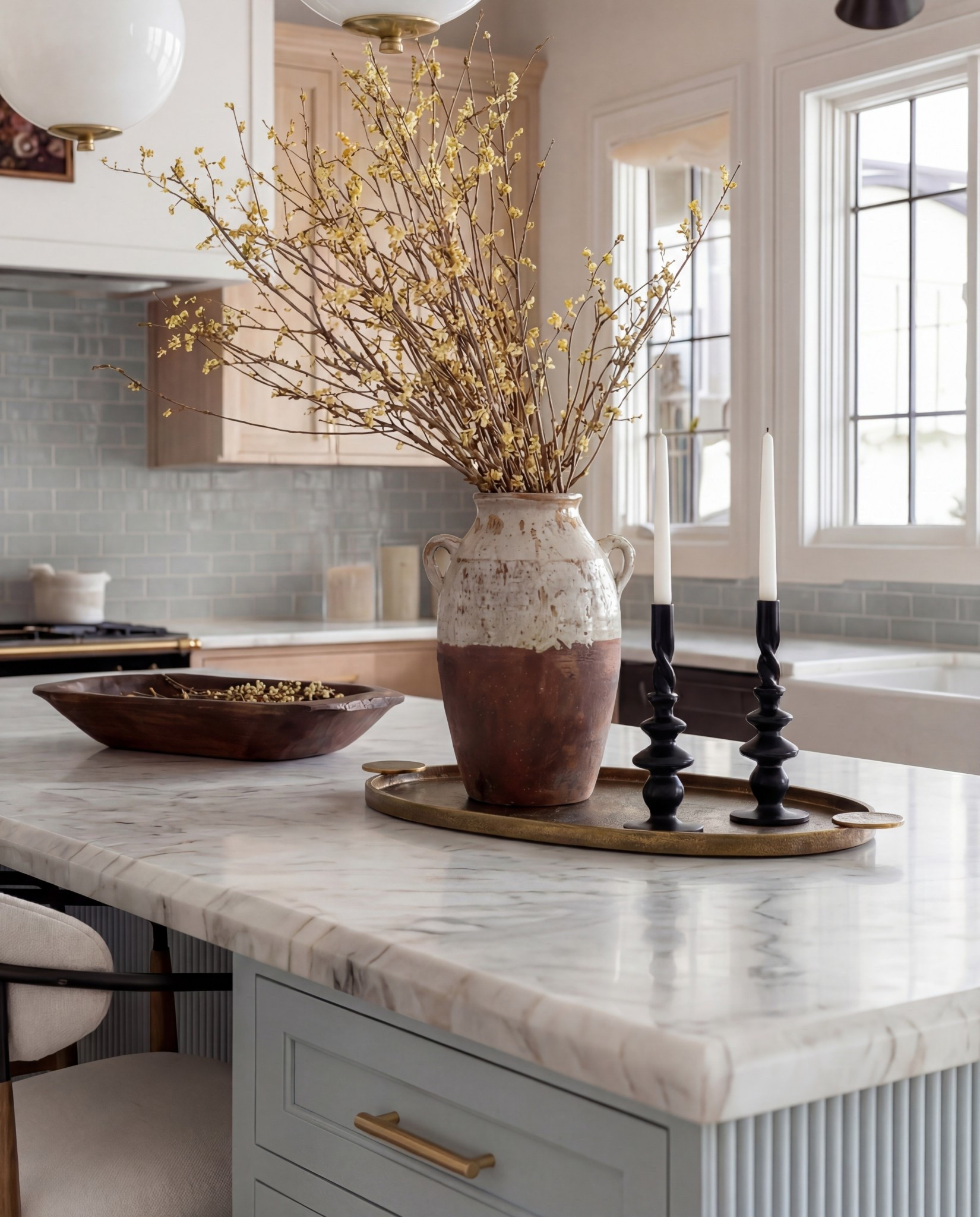 Shop the Look:
• Light blue fluted kitchen island
• Warm oak kitchen cabinets
• Brass globe pendant lights
• Marble kitchen countertop
• Neutral blue patterned runner
• Black + brass bar stools
• Soft blue subway tile backsplash
• Brown Ceramic vase with branches
• Gold kitchen faucet and hardware
•Brown bowl 
Brown floral wall art
Black candle holder

#LTKSaleAlert #LTKHome #LTKFindsUnder100