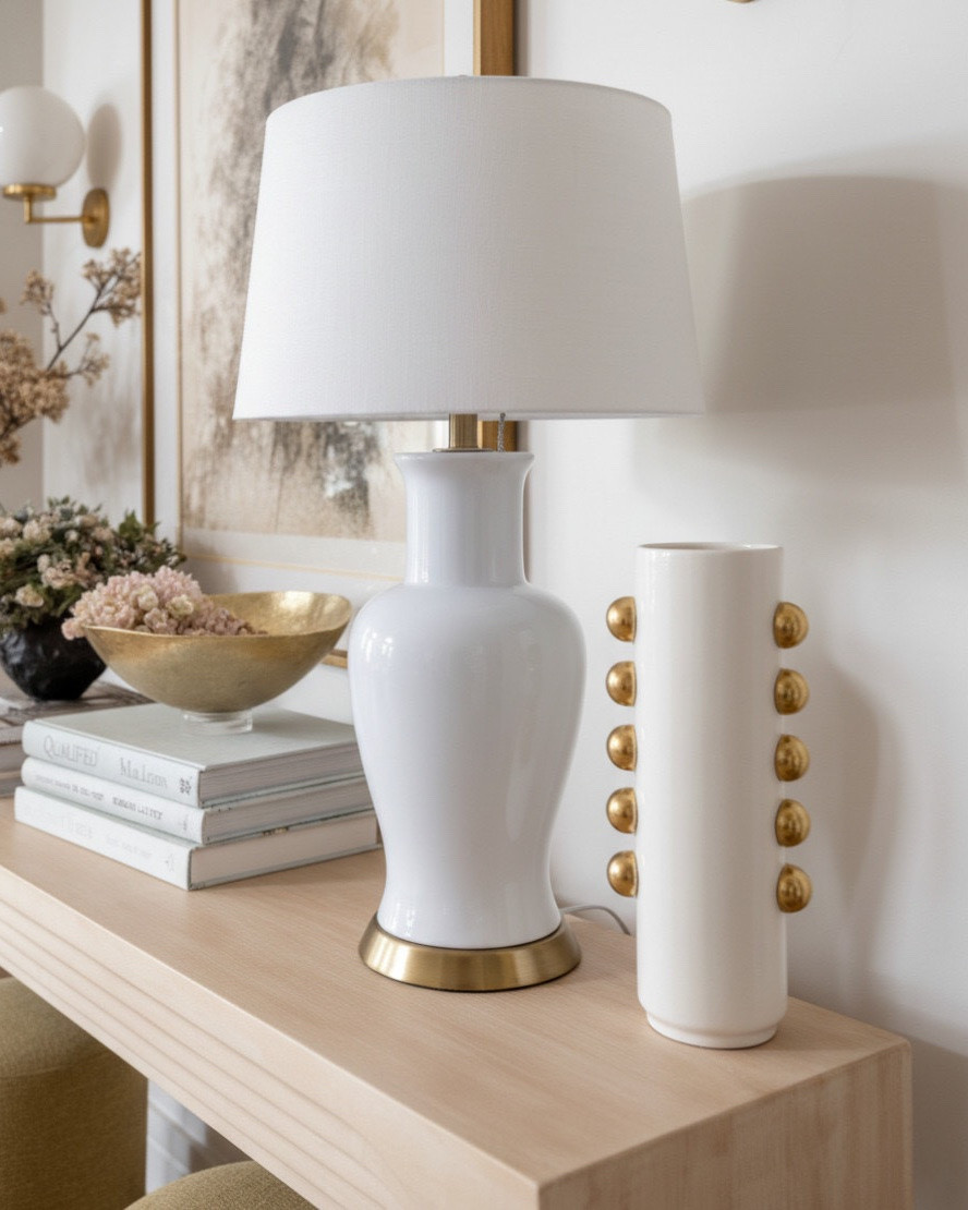 A bright and sculptural foyer layered with warm neutrals and organic textures.
The light oak console table features soft, carved arches in a natural blonde wood finish, bringing a modern coastal feel with its airy, architectural lines. Tucked beneath, a pair of round upholstered stools in a muted olive gold fabric add a pop of earthy color and soft texture to balance the wood tones.

On the console, the styling blends matte, metallic, and organic finishes: a white ceramic table lamp with brushed brass accents, a gold hammered metal bowl, and a collection of textured vases in charcoal and ivory tones. Soft faux florals in shades of nude, blush, and taupe bring a natural, curated look.

Above the table, a warm toned abstract landscape in a brushed gold frame anchors the vignette with sandy neutrals, charcoal shading, and soft brown undertones. Flanking the art, brass globe sconces with glossy white shades add a refined glow and tie in the metallic accents.

The space is grounded by light European oak floors with subtle knots and a warm, neutral wash, creating a clean, inviting entry that feels luxurious without being overdone.

✨ Shop the look:
• Light blonde oak carved console table
• Olive gold upholstered round stools
• White ceramic table lamp with brass detail
• Charcoal + ivory textured vases
• Gold hammered accent bowl
• Faux neutral florals
• Warm abstract artwork in brushed gold frame
• Brass globe wall sconces
• Natural woven basket

#LTKsale #LTKhome #LTKstyletip