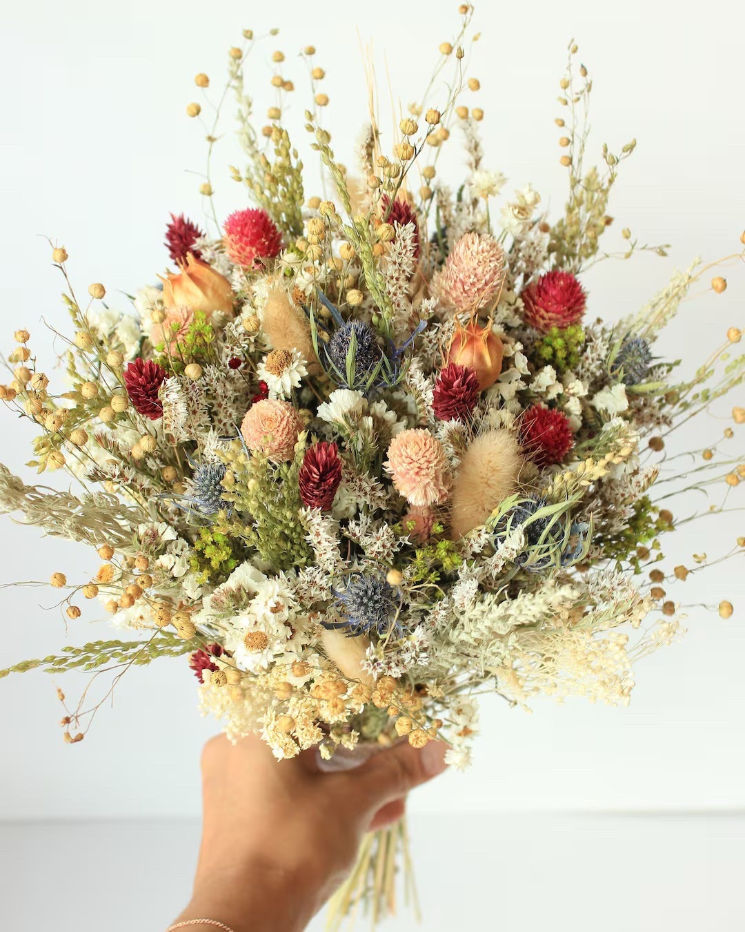 This handcrafted dried flower bouquet from Bridalwishdesign is a stunning blend of rich, seasonal tones and natural texture. Featuring blue thistle, burgundy phalaris, preserved daisy accents, hot pink globe amaranth, and soft greenery, it’s beautifully suited for fall or winter weddings, rustic celebrations, and bridal party styling. Each bouquet is thoughtfully arranged by hand, making every piece one of a kind in color balance and character. With multiple size options available, it’s easy to coordinate a cohesive look for bridesmaids, junior attendants, and the bride.

#LTKwedding #BridalBouquet #DriedFlowers #PreservedFlowers #FallWedding #WinterWedding #RusticWedding #EtsyFinds #BridalStyle

#LTKHome #LTKWedding #LTKSeasonal